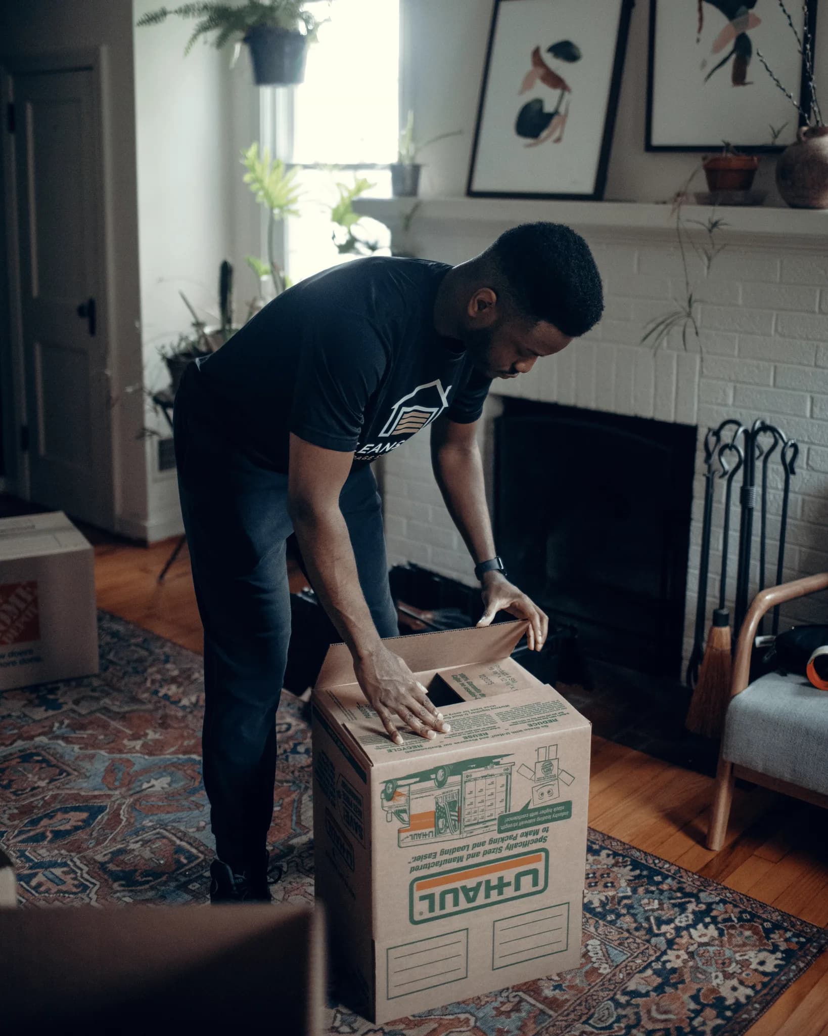 CleanSlate crew member in branded gear taping a moving box in a furnished living room