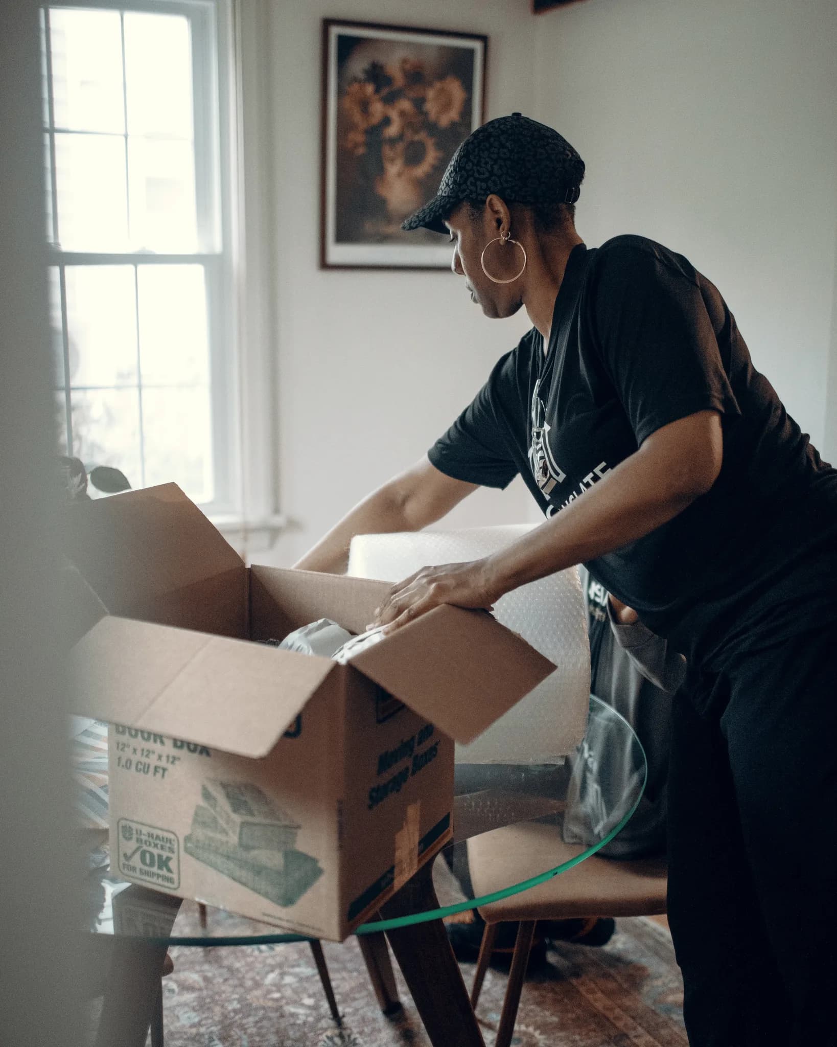 CleanSlate crew member in branded gear packing a box with bubble wrap by a window